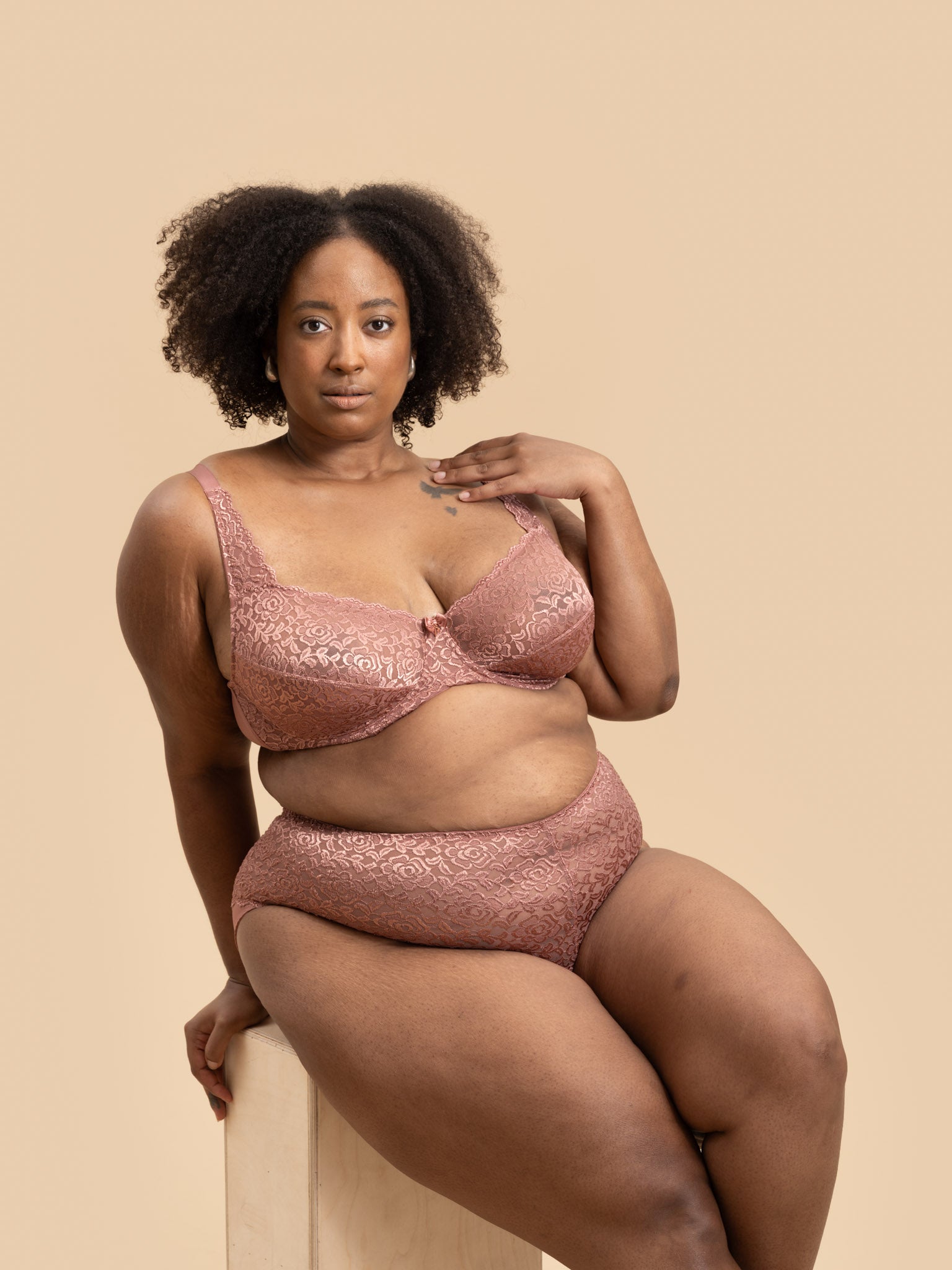 Woman wearing a pink lace lingerie set against a beige background