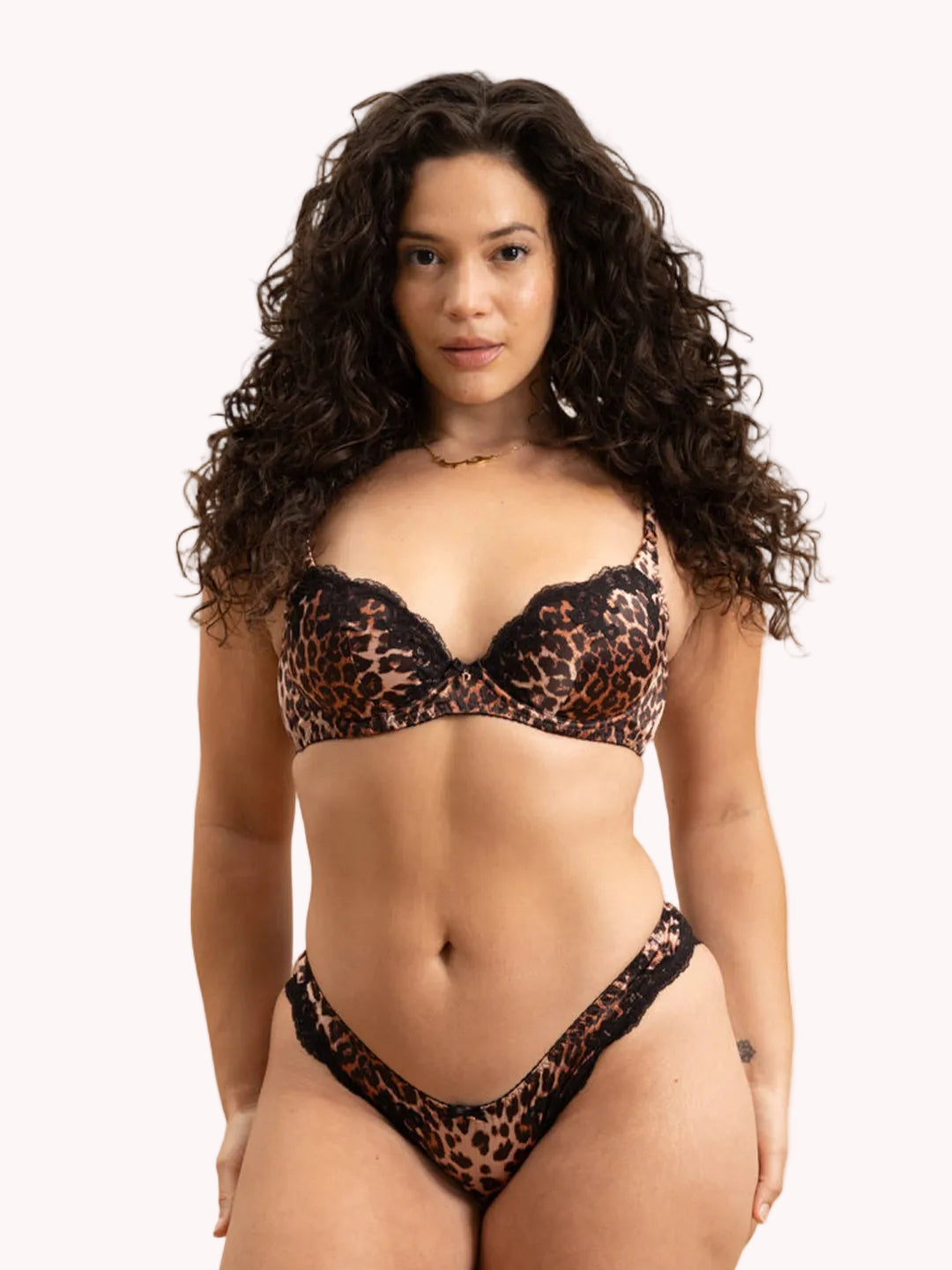 A woman modeling a leopard print and black lace two-piece lingerie set against a plain white studio background.