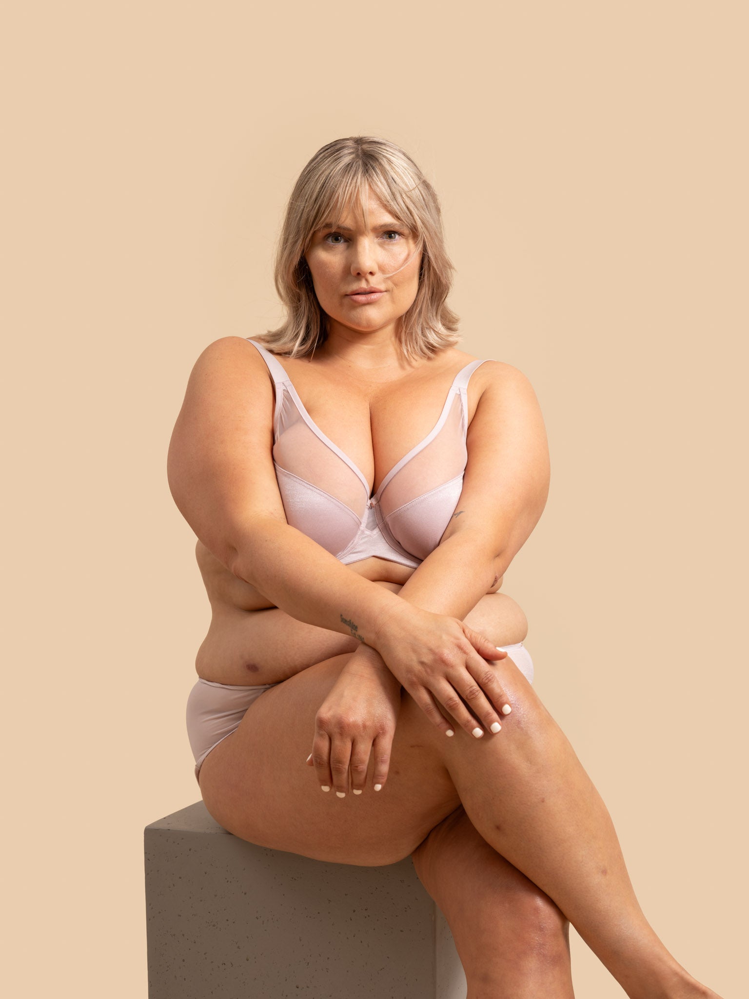 Woman wearing a light pink bra and underwear set sitting on a beige background
