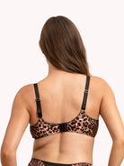 Rear view of a woman wearing a leopard-print bra with black straps and a black center band, shown against a plain light background.