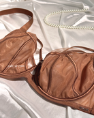 A close-up of a brown mesh and satin bra laid on white satin fabric, with a pearl necklace prop in the background.
