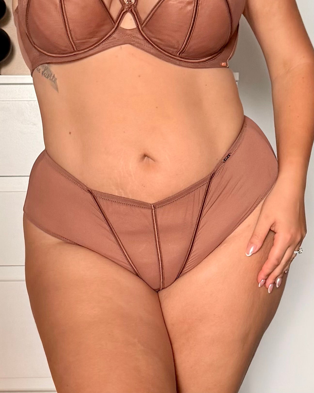 A close-up of a model wearing a two-piece lingerie set in a dusty rose or mauve-brown shade, featuring a strappy bra top and matching high-waisted briefs.