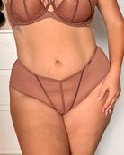 A close-up of a model wearing a two-piece lingerie set in a dusty rose or mauve-brown shade, featuring a strappy bra top and matching high-waisted briefs.
