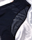 Close-up of a black high-waisted bikini bottom laid flat on a white satin fabric background, showing the sheer mesh side panel and black trim.